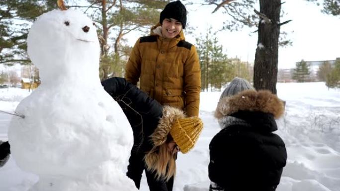 幸福的家庭妈妈，爸爸和儿子在冬季城市公园堆雪人。