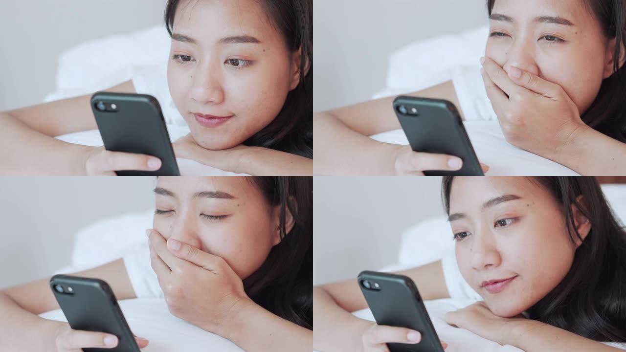 亚洲女性正在使用触摸屏智能手机，用手捂脸在家里的床上打哈欠。