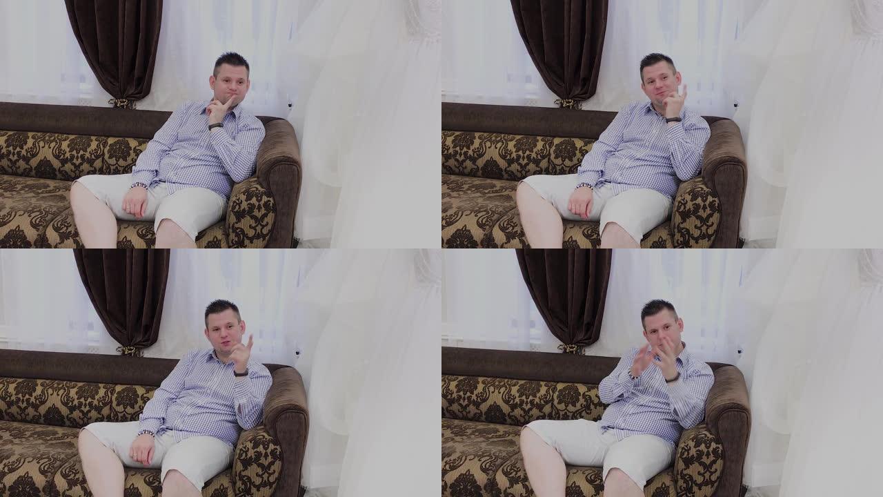 一个情绪激动的男人坐在婚礼沙龙的沙发上，对他的女人展示的衣服做出反应