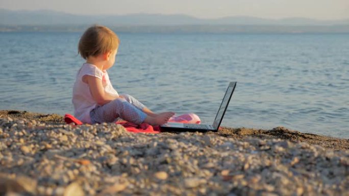 蹒跚学步的孩子坐在海边，拿着笔记本。工作和假期相结合的新一代人。学龄前背景。教育革命。发展创造力。新