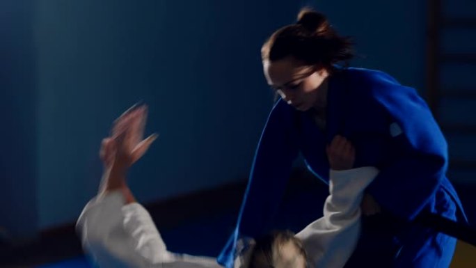 漂亮的年轻女子在健身房打架，柔道比赛。在榻榻米上捕获、投掷和痛苦的技术。肖像视图。