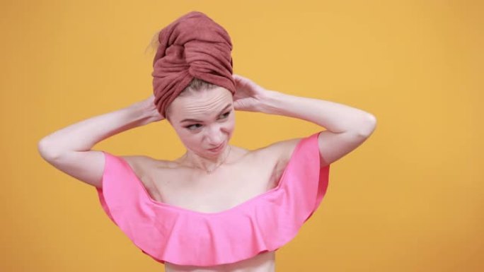 年轻女孩头上带着毛巾在孤立的橙色背景上显示出情感