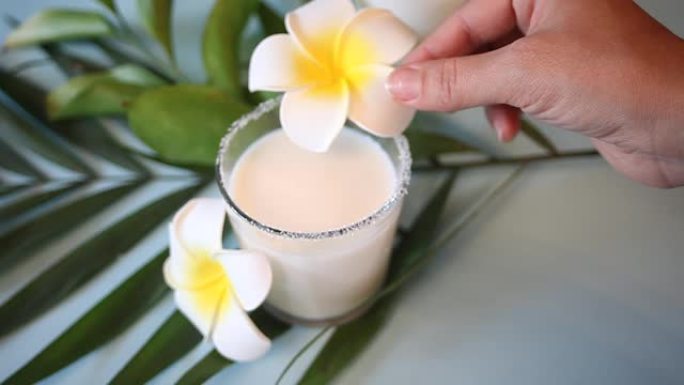 女人的手把鸡蛋花鸡蛋花放在椰奶杯上。背景上的棕榈叶。
