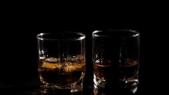 豪华威士忌。冰块掉落成带有金色威士忌的玻璃杯，放在装有威士忌和冰的玻璃附近的黑色桌子上。不倒翁苏格兰