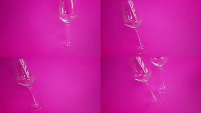 几个酒杯在坚实的粉红色背景上滚动并碰撞，自上而下拍摄。
