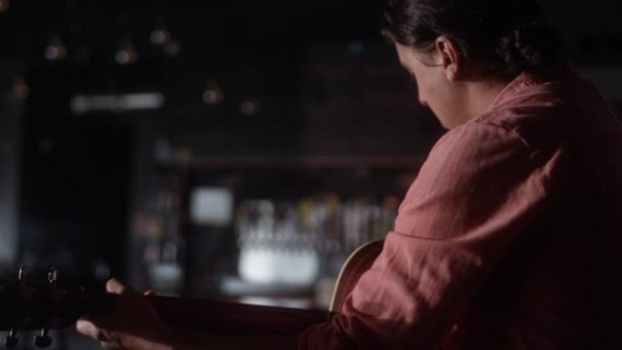 一名拉丁裔男子在昏暗的酒吧里从后面弹吉他，相机平移到他的脸上