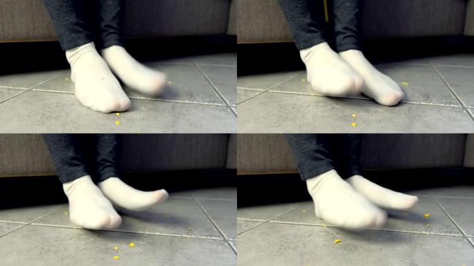 女人在沙发上吃饭，在地板上碎玉米片。腿和地板特写。