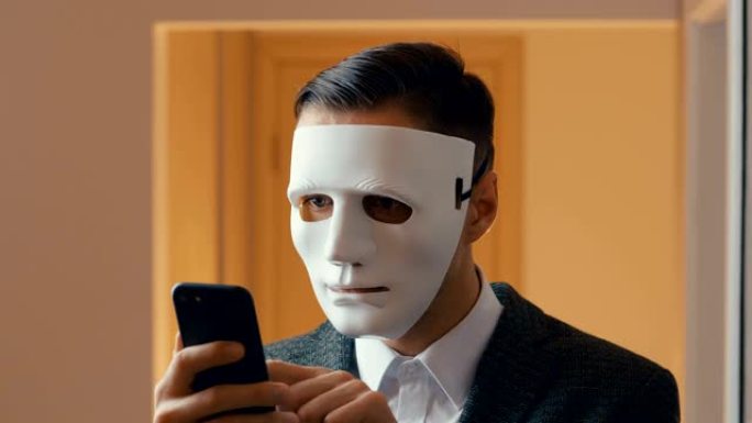 蒙面匿名罪犯使用智能手机。男人写勒索信息。