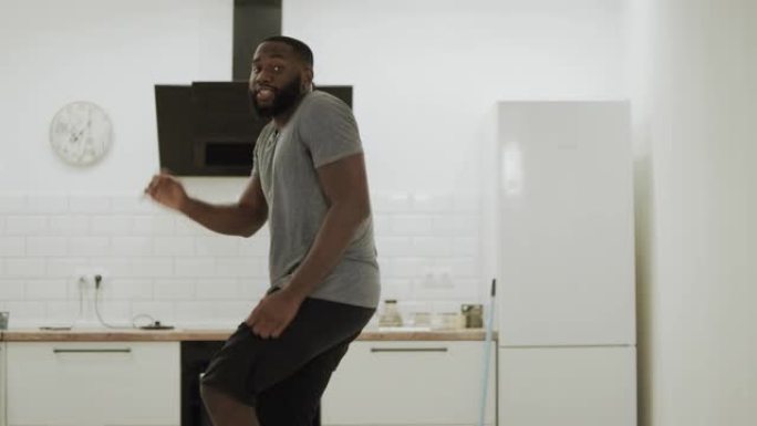 快乐的黑人在开放式厨房拍手。快乐的年轻人在家跳舞
