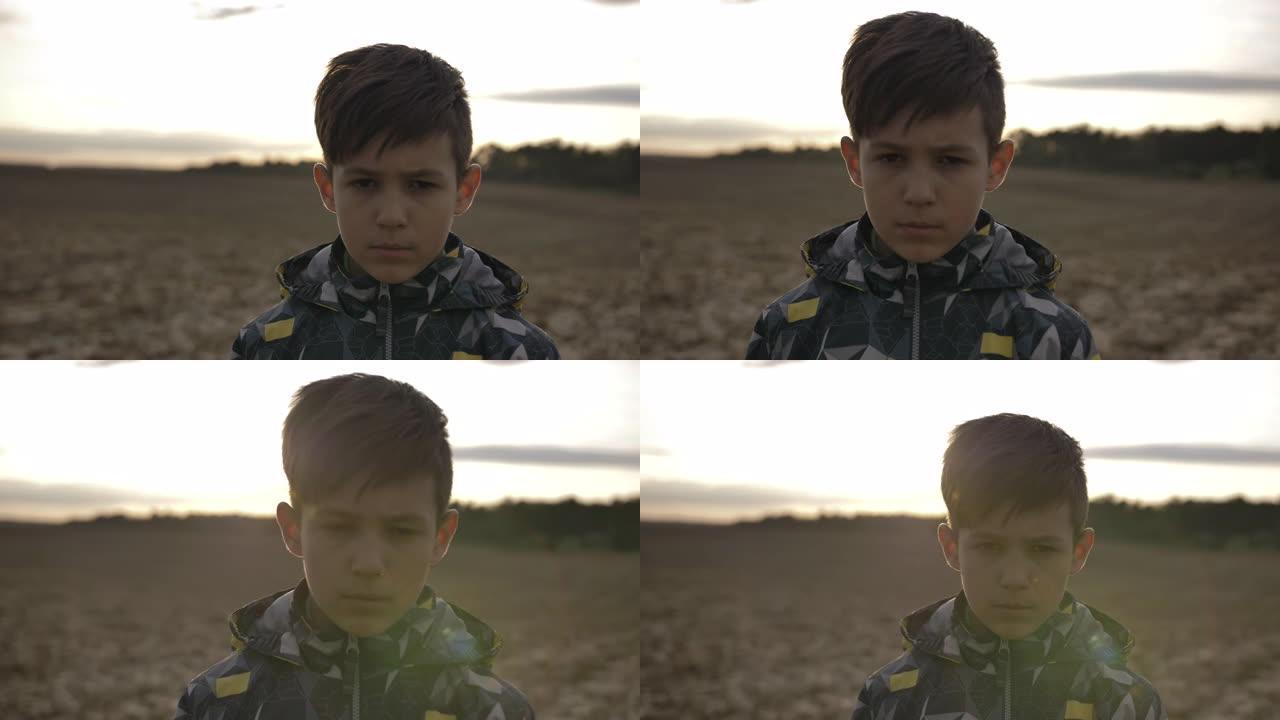 日落时看着相机的冒犯悲伤男孩的肖像