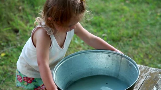 小女孩试图举起装满水的金属盆