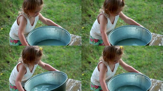 小女孩试图举起装满水的金属盆