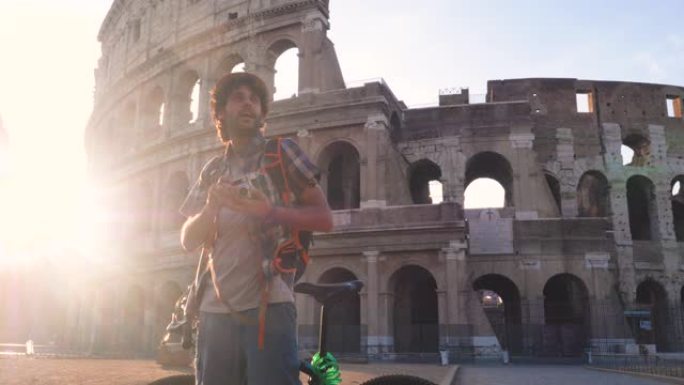 日出时，穿着衬衫和帽子的快乐年轻人游客在意大利罗马罗马斗兽场用老式相机拍照。