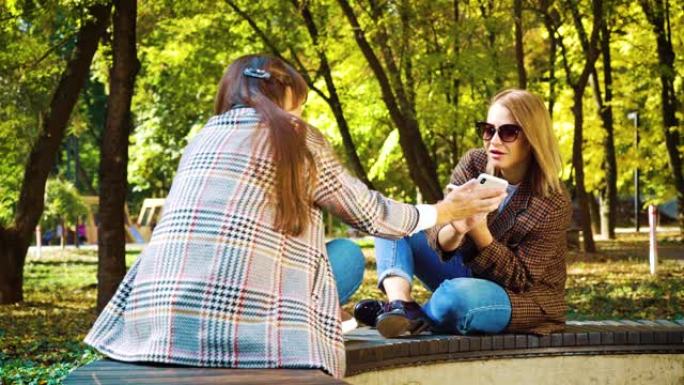 和蔼可亲的女孩坐在秋季公园使用智能手机应用程序