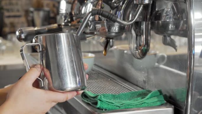 咖啡师在发泡罐中蒸牛奶，为咖啡店顾客准备饮料
