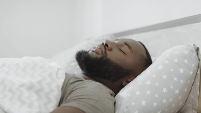 黑人早上睡在床上。年轻人用枕头遮头。