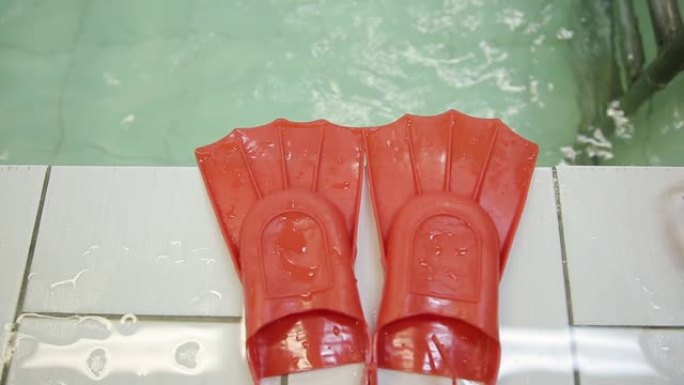 游泳用鳍。红色鳍状肢躺在水的背景上的游泳池边缘