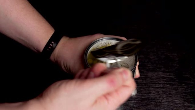 男性双手在黑色背景上打开金属锡罐。