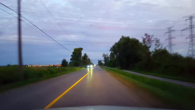 开车穿过乡村，接近地平线上的城市灯光。驾驶视点POV在早上或晚上驶向进入城市极限。