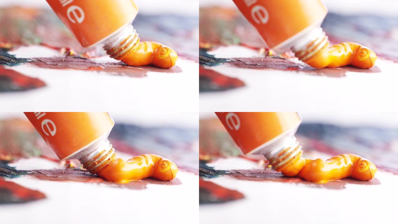 从画好的画布上的小管上压出的橙色油画的特写镜头。行动。艺术与绘画概念