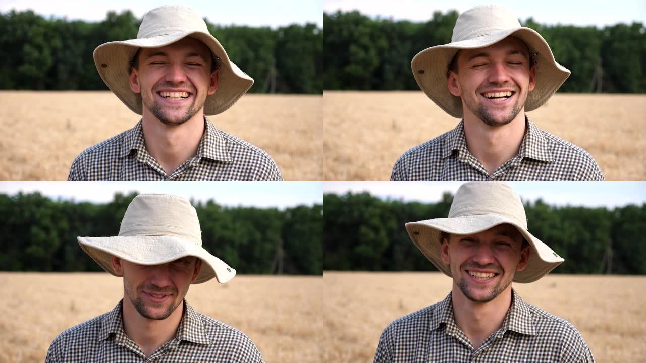 戴着帽子的快乐微笑的农艺师的肖像在麦田模糊的背景下看着相机。年轻的笑农站在大麦草地上。农业商业概念。