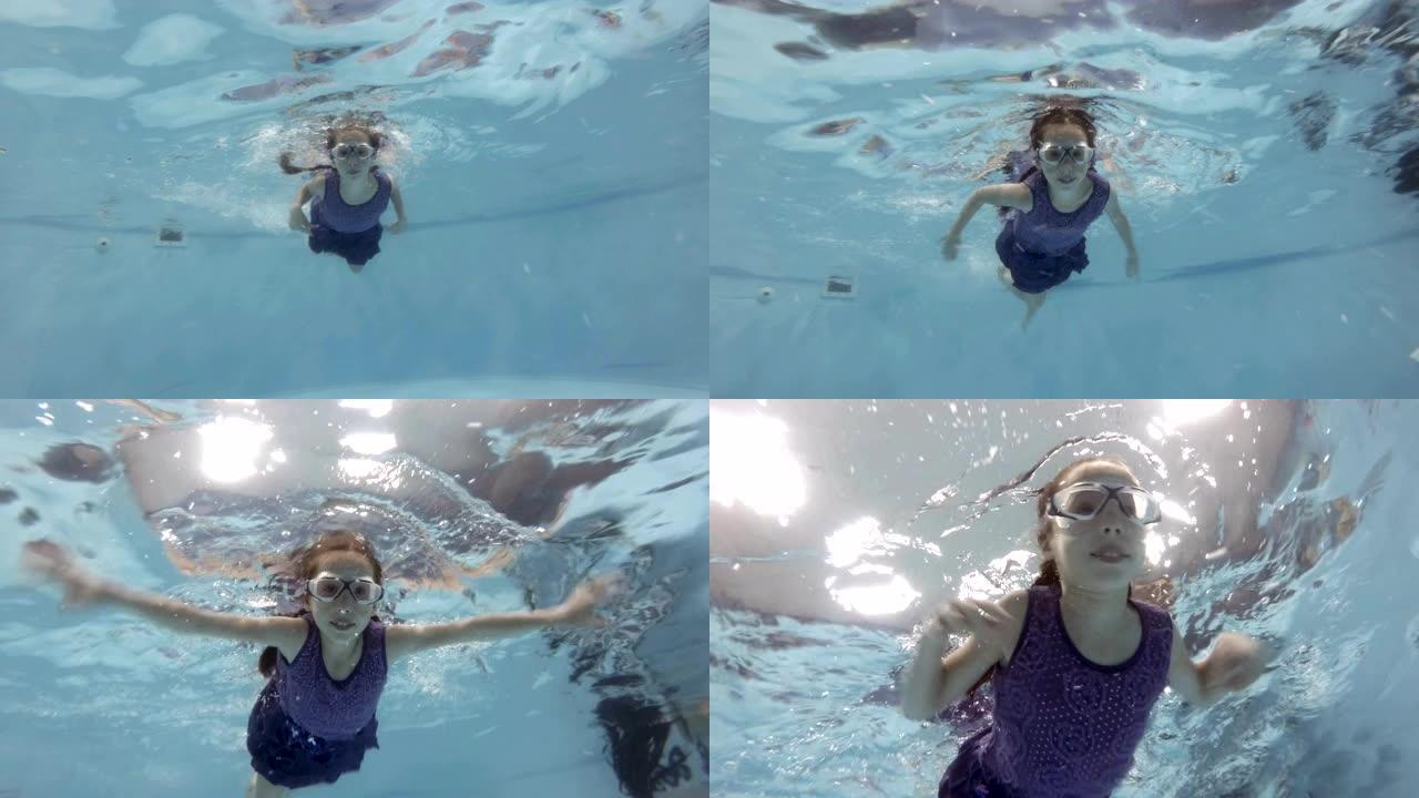 一个运动的小女孩戴着泳镜在游泳池水下游泳，看着相机。特写。底视图。慢动作。4K。