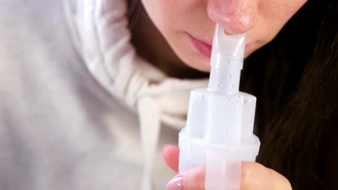 使用雾化器和吸入器进行治疗。年轻女子通过鼻子的吸入器喷嘴吸气。特写鼻子。