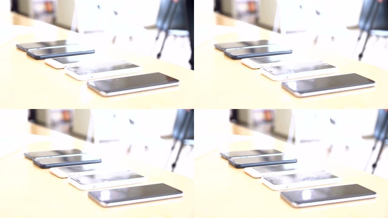 注意桌子上的桌子连续摆放几部手机，年轻人的手从桌子上拿起手机径向相机跟踪