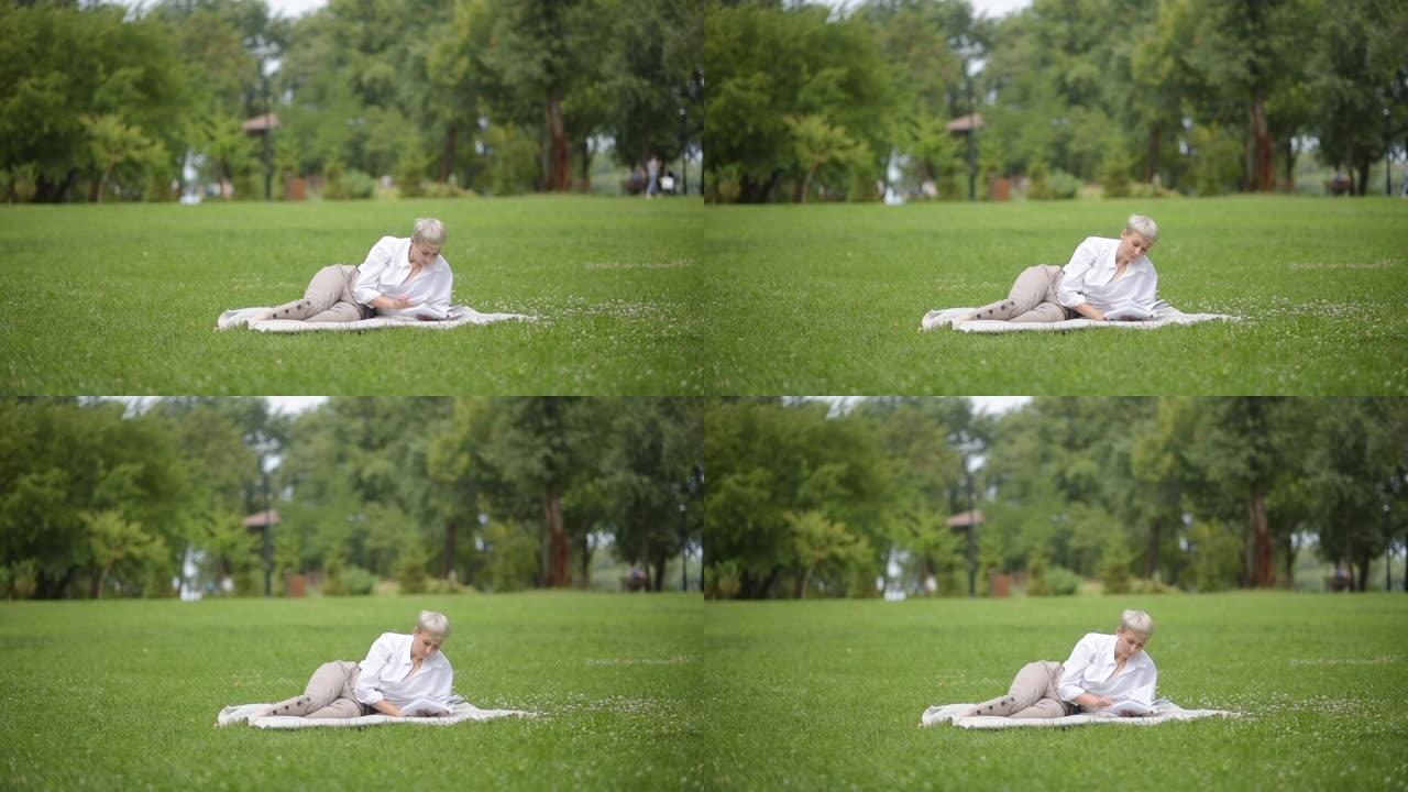美女金发在公园的草地上看书