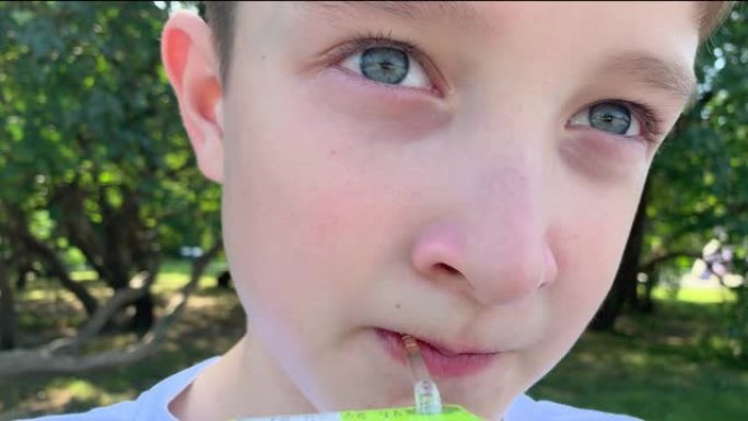 一个年轻的青春期白人男孩坐在夏季城市公园里，用纸果汁包装的吸管喝果汁，特写镜头，外卖快餐概念