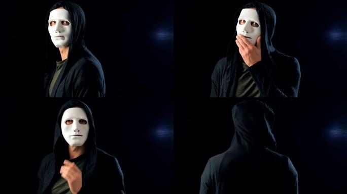 匿名男子戴着白色面具遮住脸，戴着黑色兜帽转身看着相机。黑色深色背景。秘密组织成员的概念