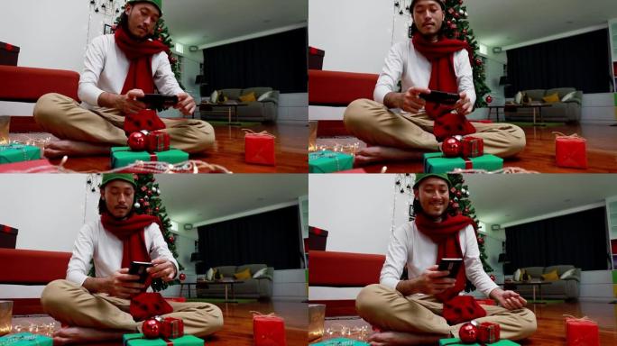 微笑亚洲男子使用手机拍摄照片礼品盒，并上传到互联网在家里的客厅有一棵圣诞树的背景。圣诞节庆祝概念。