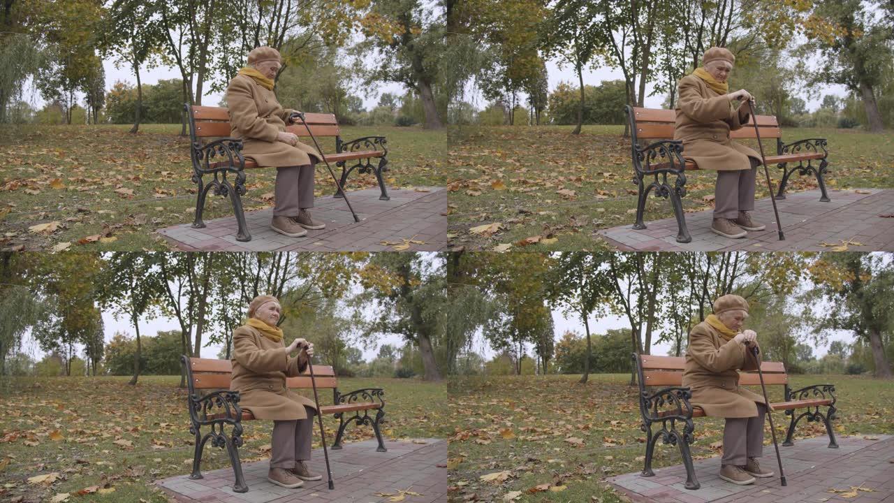 老妇人倚着拐杖独自坐在公园长椅上，悲伤的回忆，健康状况不佳