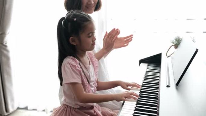 亚洲母亲和女儿一起弹钢琴的慢动作镜头。母亲带着幸福和微笑教导女儿，拍手。