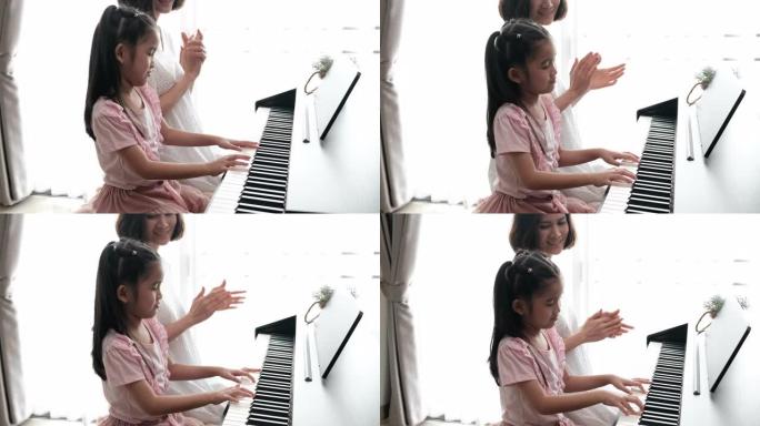 亚洲母亲和女儿一起弹钢琴的慢动作镜头。母亲带着幸福和微笑教导女儿，拍手。