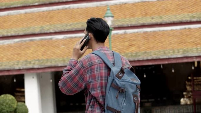 独自旅游的亚洲人在泰国的寺庙里走路，和朋友用手机聊天。亚洲男子博客愉快享受休闲生活方式旅游。