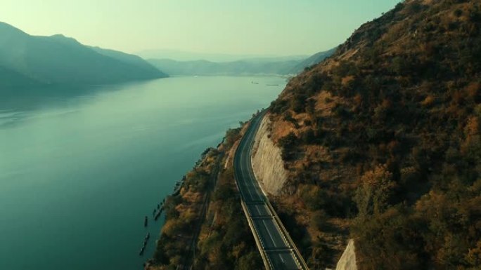 白色卡车和汽车在山附近过桥。一边是山，另一边是美丽的蓝色多瑙河。