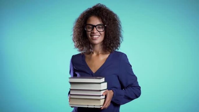 工作室里戴着蓝色背景眼镜的非洲学生拿着一堆图书馆的大学书籍。女孩笑了，她很高兴毕业。