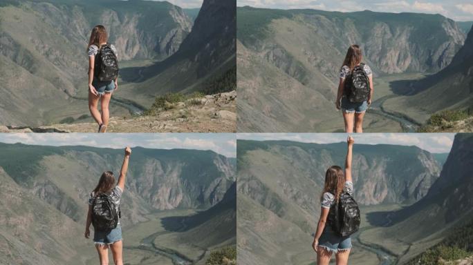 一个背着背囊的女旅行者爬到山顶，举起手来，有一种潇洒成功的感觉。后视图
