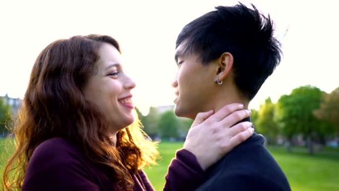 年轻的亚洲高加索夫妇在日落时在公园接吻，阳光照在后面