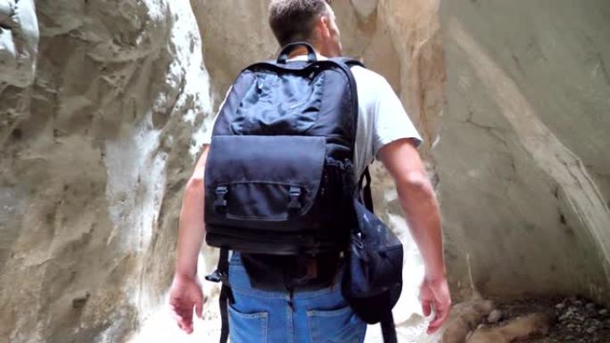 面目全非的年轻人背着背包走过狭窄的峡谷。探索岩石峡谷和欣赏风景的男性徒步旅行者。旅行或主动休息的概念