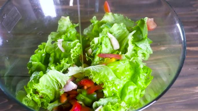 厨师用橄榄油浇灌沙拉。一股稀薄的油流倒在一个大玻璃杯里的新鲜天然蔬菜沙拉上。健康的饮食食品。慢动作。