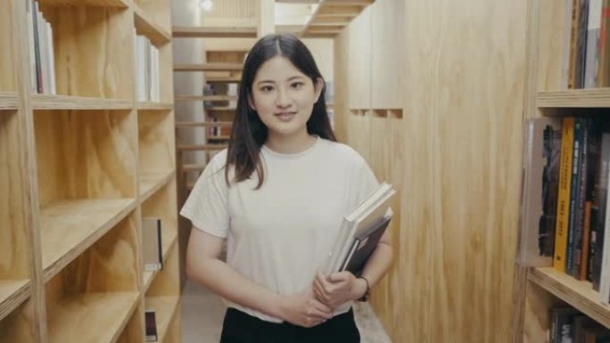 一个可爱的年轻亚洲女学生在书架之间行走的肖像 (慢动作)