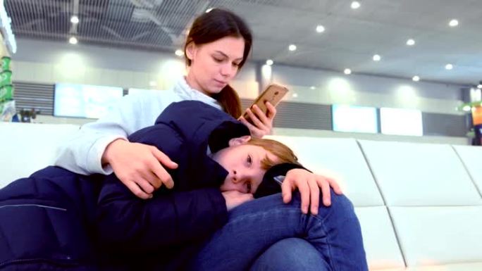 女人带着疲惫的儿子在机场大厅的手机上在线登记。