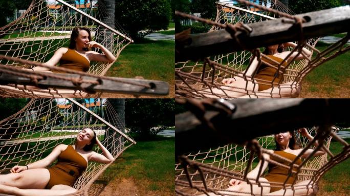 一个穿着连体泳衣的年轻美女躺在热带植物周围的吊床上休息