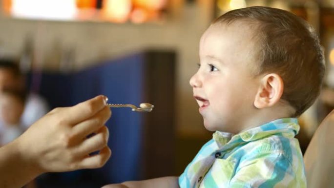 母亲在餐馆用婴儿勺子给婴儿食物，孩子心甘情愿地吃东西。4k。