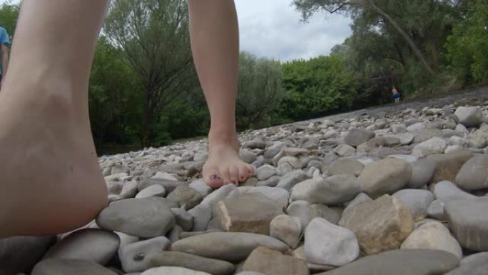 成年妇女在河岸的鹅卵石上赤脚行走的特写镜头