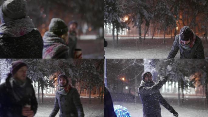 一群快乐的朋友手里拿着纸咖啡杯在降雪下行走，玩雪玩得开心。人们用热饮料热身，在冬夜闲逛。圣诞节和新年
