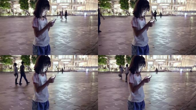 亚洲女孩晚上在购物中心使用智能手机。