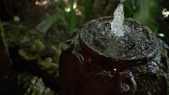 绿色花园中的慢动作水罐喷泉